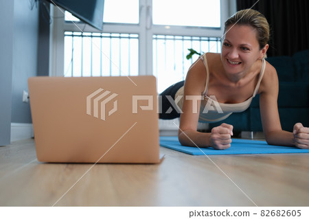 Young woman standing in plank on floor in front of laptop 82682605