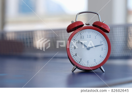 Red alarm clock standing on tennis table closeup 82682645