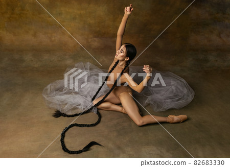 Breathtaking portrait of beautiful female ballet dancer, tender ballerina posing on transparent fabric element isolated over studio background 82683330