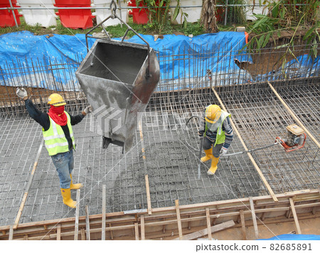 KUALA LUMPUR, MALAYSIA -AUGUST 8, 2018: Group of construction workers pouring wet concrete using the mobile crane bucket at the construction site. KUALA LUMPUR, MALAYSIA -AUGUST 8, 2018: Group of construction workers pouring wet concrete using the mobile crane bucket at the construction site. 82685891
