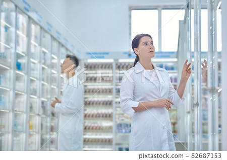 Woman looking closely at pharmacy shelves and employee Woman looking closely at pharmacy shelves and employee 82687153
