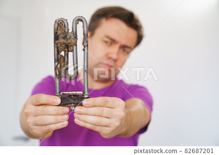 repairman of washing machine holds old tubular electric heater. selective focus repairman of washing machine holds old tubular electric heater. selective focus 82687201
