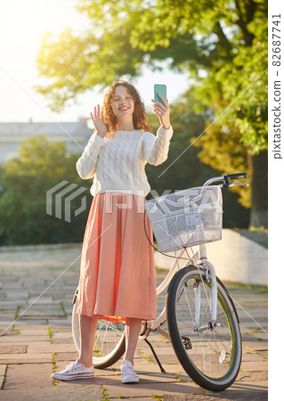 A dark-haired young girl with a bike making selfie in the park 82687741