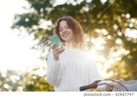 A young girl in a park with a smartphone in hands A young girl in a park with a smartphone in hands 82687747