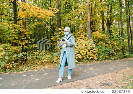 Muslim woman with hijab is wearing face mask outdoors. Coronavirus, health care and pandemic concept. Space for advertisement 82687879