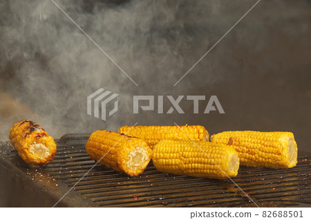 Fresh corn on the grill grate and a big cloud of smoke in the background. 82688501