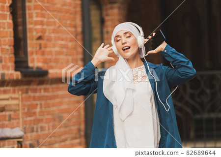 Portrait of young arabian muslim woman listening music with headphone and dancing. Feminism, woman independence and leisure concept. 82689644