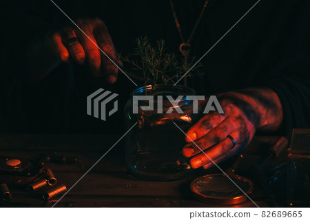 hands of sorcerer alchemist prepare a magic potion poison with herbs in flask at table hands of sorcerer alchemist prepare a magic potion poison with herbs in flask at table 82689665