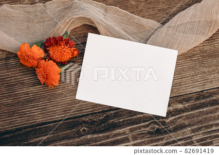 Autumn wedding still life scene. Blank greeting card mock-up. Floral composition. Orange tagetes flowers on old wooden table background. Flat lay, top view. Halloween, Dia de los Muertos holiday. Autumn wedding still life scene. Blank greeting card mock-up. Floral composition. Orange tagetes flowers on old wooden table background. Flat lay, top view. Halloween, Dia de los Muertos holiday. 82691419