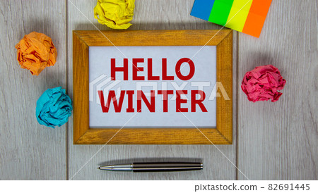 Wooden frame with inscription 'hello winter' on beautiful wooden table, colored paper, metalic pen. Concept. 82691445