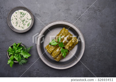 Top view dolma, parsley, saucepan with sour cream on ceramic color graphite plate Top view dolma, parsley, saucepan with sour cream on ceramic color graphite plate 82693451