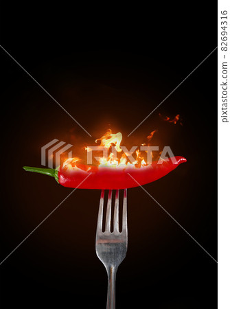 Red chili peppers on a fork in flame. Hot red chili peppers on a fork in flame on a black background. 82694316