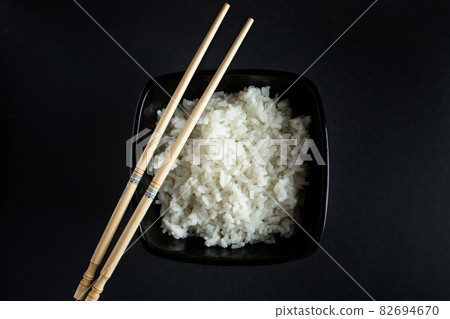 Bowl with boiled rice on a black background. Asian food and bamboo chopsticks. Bowl with boiled rice on a black background. Asian food and bamboo chopsticks. 82694670
