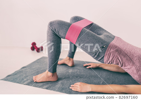 Fitness woman leg workout with resistance band exercise for thighs and glutes hip bridge abduction. Yoga fit girl strength training on floor at home. Pink accessory 82697160