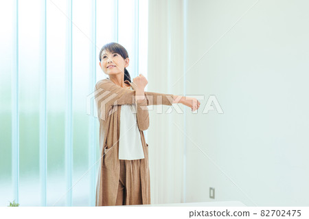 Middle-aged woman stretching in the room Middle-aged woman stretching in the room 82702475