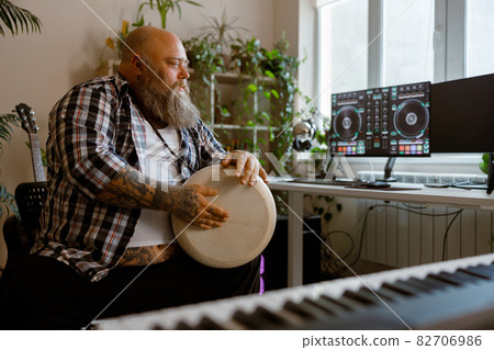 Talented man plays drum sitting at workplace with computer monitors in studio 82706986