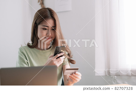 Cropped image of smiling millennial woman holding smartphone and banking credit card, involved in online mobile shopping at home, happy female shopper purchasing goods or services in internet store Cropped image of smiling millennial woman holding smartphone and banking credit card, involved in online mobile shopping at home, happy female shopper purchasing goods or services in internet store 82707328