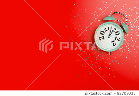 New Year 2022 banner background concept. 2021 changes to 2022 on an alarm clock on a red background with festive glitter on New Year's Eve and Christmas. 82709335