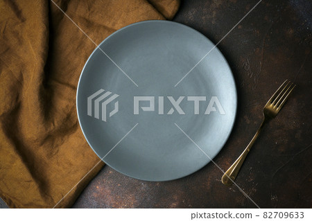 Empty plate on a dark background. Empty gray ceramic plate with a knife and fork for food and dinner on a dark beautiful background. Empty plate on a dark background. Empty gray ceramic plate with a knife and fork for food and dinner on a dark beautiful background. 82709633