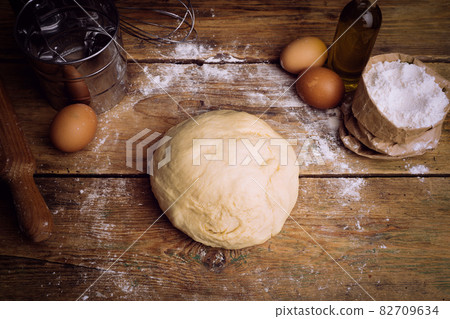 Pizza dough cooking in the home kitchen. Homemade dough for bread, pizza, pastries and rolls. Dough ingredients (flour, eggs, butter) on a wooden rustic background 82709634