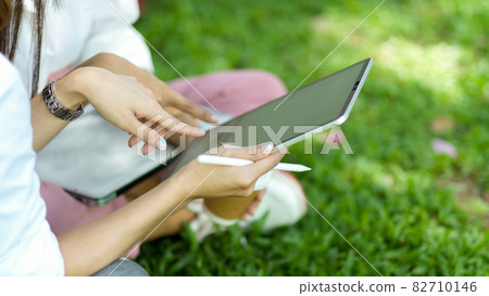 Female college student and a friend watching a funny video on a digital tablet at park 82710146