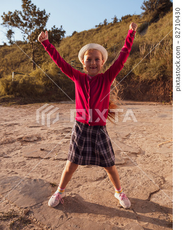 Happy little girl with long hair portrait jumping on nature background windy day. Cute kid walking alone in autumn park. 82710430