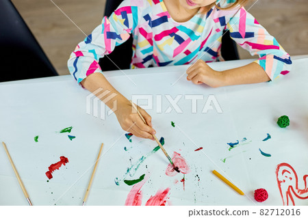 Cute child sitting at the table and drawing red heart on white paper Cute child sitting at the table and drawing red heart on white paper 82712016