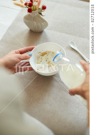 Female hand holding bottle pouring milk in cereal granola flakes bowl Female hand holding bottle pouring milk in cereal granola flakes bowl 82712018
