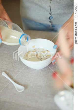 Female hand holding bottle pouring milk in cereal granola flakes bowl Female hand holding bottle pouring milk in cereal granola flakes bowl 82712020