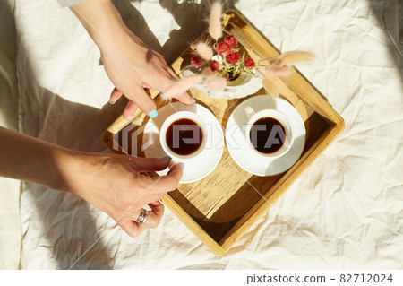 Woman sitting on the bed, and drink coffee during the morning sunlight Woman sitting on the bed, and drink coffee during the morning sunlight 82712024