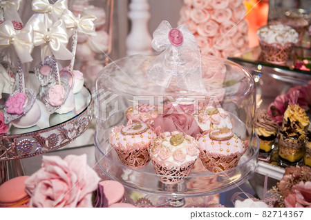 Delicious desserts at the wedding candy bar in the buffet area: muffins decorated with angels, cameo, sugar rosebuds and gold dye. 82714367