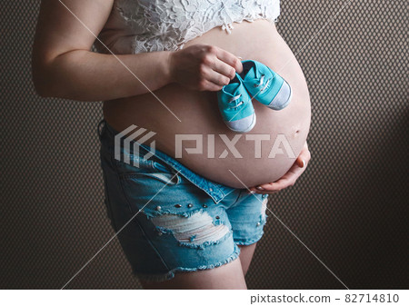 Hands of a pregnant girl hold belly and small baby booties, awaiting the birth of a baby Hands of a pregnant girl hold belly and small baby booties, awaiting the birth of a baby 82714810