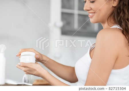 Unrecognizable Young Lady Holding Facial Cream Jar Standing In Bathroom Unrecognizable Young Lady Holding Facial Cream Jar Standing In Bathroom 82715304
