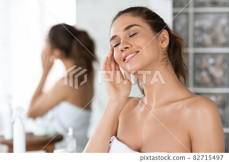 Female With Eyes Closed Applying Cream On Face In Bathroom 82715497