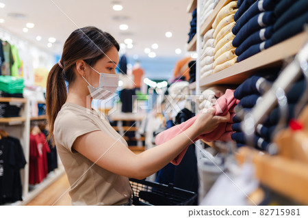 Asian woman wearing a protective face mask buying cloth in store Asian woman wearing a protective face mask buying cloth in store 82715981