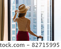 Portrait rear view of woman standing close to the window, looking outside in hotel room after check-in 82715995