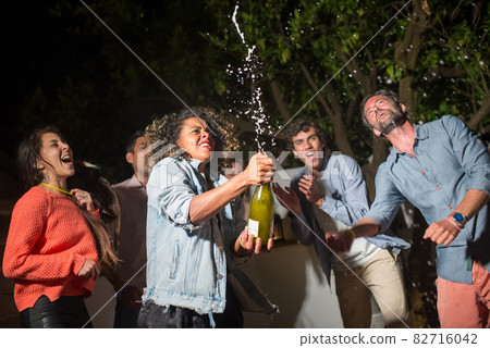 Young curly woman opening champagne at party Young curly woman opening champagne at party 82716042