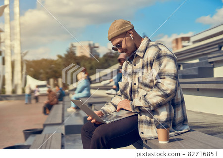 Young hipster man sits outdoor with coffee while checking email, working, blogging, studying online  82716851