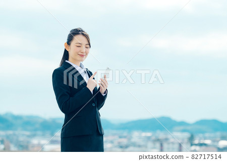 A young smiling business woman in a suit with a smartphone 82717514