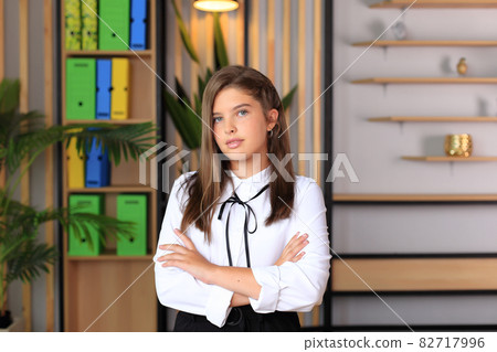 Young beautiful girl in office style looks at the camera. A teenager in school clothes in the office. Young teacher in a school class. Business girl in the office 82717996