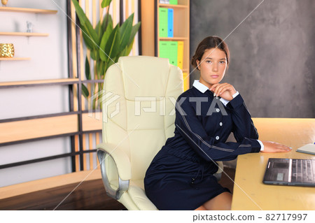 Young beautiful girl in office style looks at the camera. A teenager in school clothes in the office. Young teacher in a school class. Business girl in the office 82717997