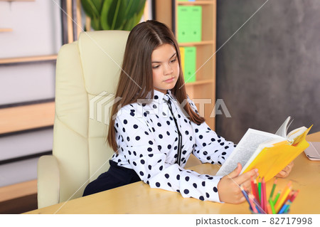 Portrait of a girl in a school uniform with a book in her hands. The child reads a textbook. Preparing a schoolgirl for a school lesson or exam 82717998