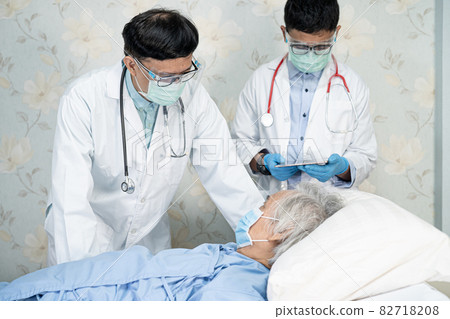 Asian doctor team check old senior lady patient for disease to motivation new normal to treat infection Covid-19 Coronavirus at hospital ward. 82718208