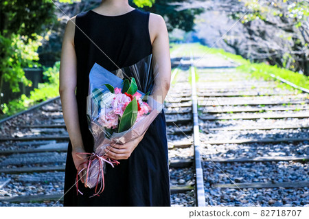 A woman holding a bouquet, an abandoned railroad track shining through the sunlight 82718707