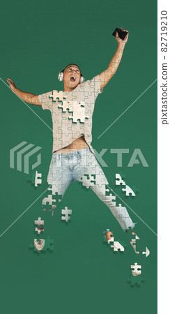 Full-length creative collage of man listening to music in a jump isolated over green background. Portrait consist of puzzle pieces Full-length creative collage of man listening to music in a jump isolated over green background. Portrait consist of puzzle pieces 82719210