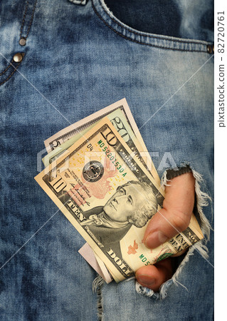 Hand holds US dollar banknotes in jeans rip hole Hand holds US dollar banknotes in jeans rip hole 82720761
