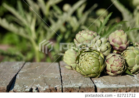 Fresh artichoke globes on wooden table in garden 82721712