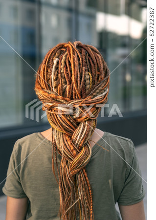 Beautiful girl with a long braid of red dreadlocks. The girl stands with her back to the camera. Close-up. 82722387