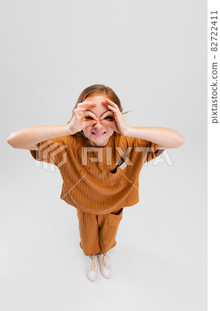 Portrait of little Caucasian girl, child posing isolated over gray studio background. Looking through hand glasses 82722411