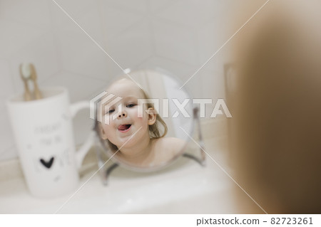 reflection in the mirror of a little funny girl washing hands and face in the bathroom 82723261